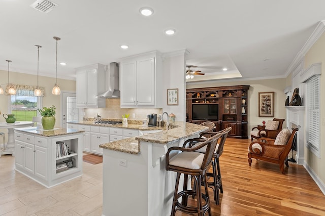 kitchen with visible vents, stainless steel gas stovetop, wall chimney exhaust hood, and white cabinetry