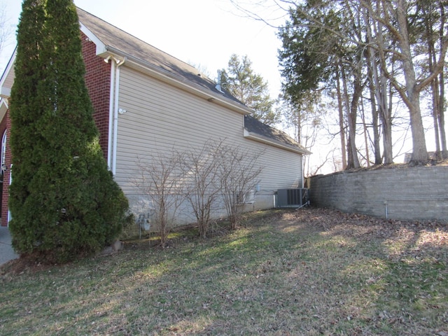 view of property exterior featuring a yard, brick siding, fence, and central AC unit