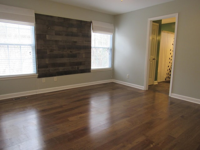 empty room with a healthy amount of sunlight, baseboards, visible vents, and dark wood-style flooring