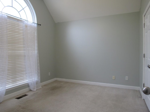 carpeted spare room featuring baseboards, visible vents, and vaulted ceiling