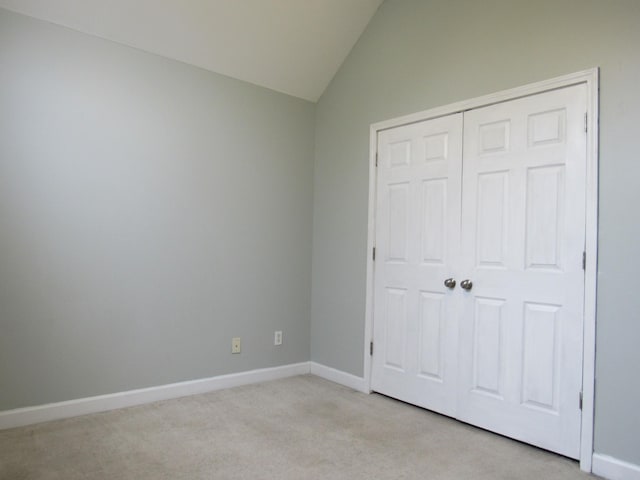 unfurnished bedroom featuring vaulted ceiling, a closet, baseboards, and light colored carpet