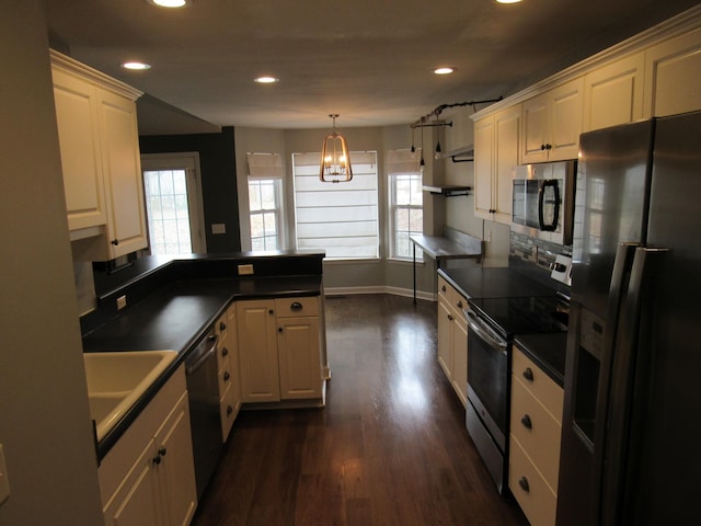 kitchen featuring a peninsula, a healthy amount of sunlight, dark countertops, and stainless steel appliances