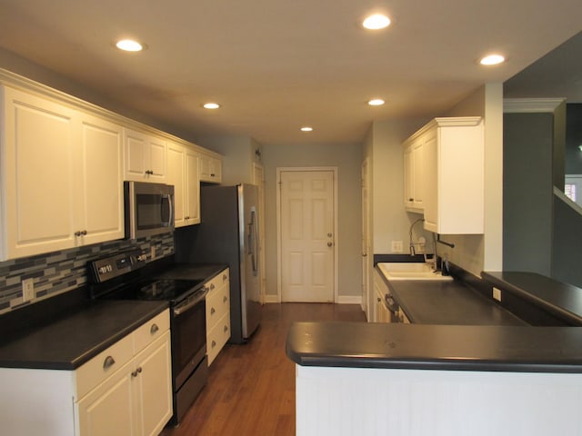 kitchen with appliances with stainless steel finishes, dark countertops, a sink, and white cabinets