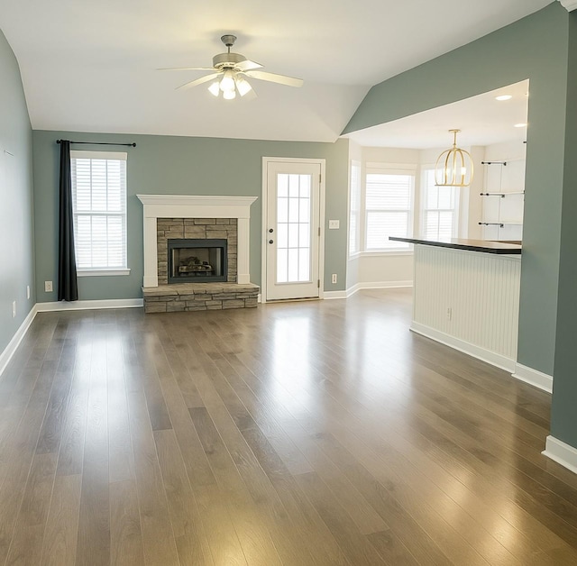 unfurnished living room with baseboards, a fireplace, vaulted ceiling, ceiling fan with notable chandelier, and dark wood-type flooring