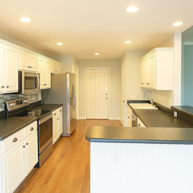 kitchen featuring white cabinets, a sink, dark countertops, stainless steel appliances, and light wood-style flooring