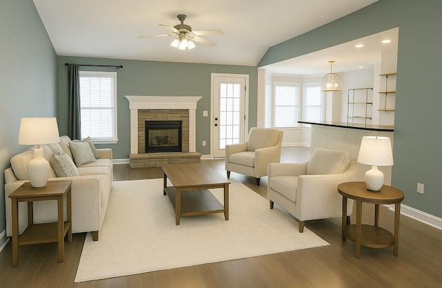 living area with baseboards, a stone fireplace, wood finished floors, lofted ceiling, and ceiling fan