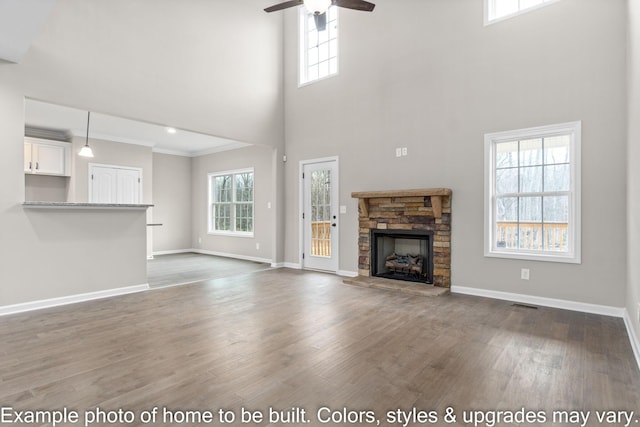 unfurnished living room featuring baseboards, ornamental molding, wood finished floors, and a stone fireplace