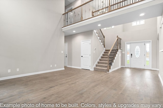 interior space featuring recessed lighting, a high ceiling, wood finished floors, baseboards, and stairs