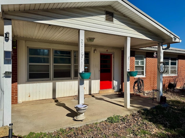 view of exterior entry with brick siding and a porch