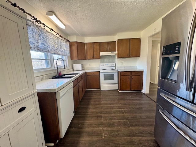 kitchen with under cabinet range hood, white appliances, a sink, light countertops, and dark wood finished floors