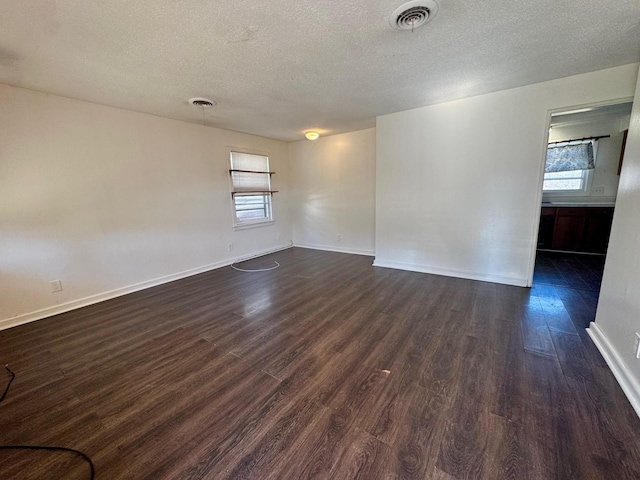 unfurnished room featuring dark wood-style floors, visible vents, and baseboards