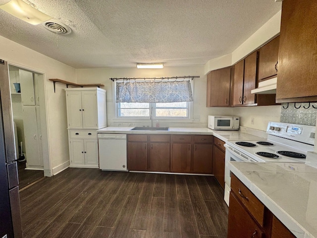 kitchen with dark wood finished floors, visible vents, light countertops, white appliances, and under cabinet range hood