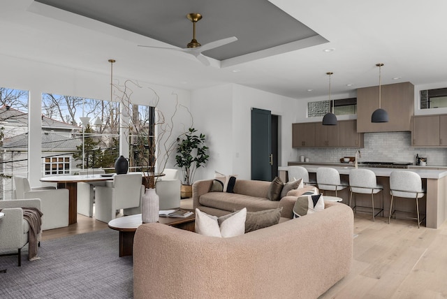 living area featuring light wood-style floors, a tray ceiling, recessed lighting, and a ceiling fan