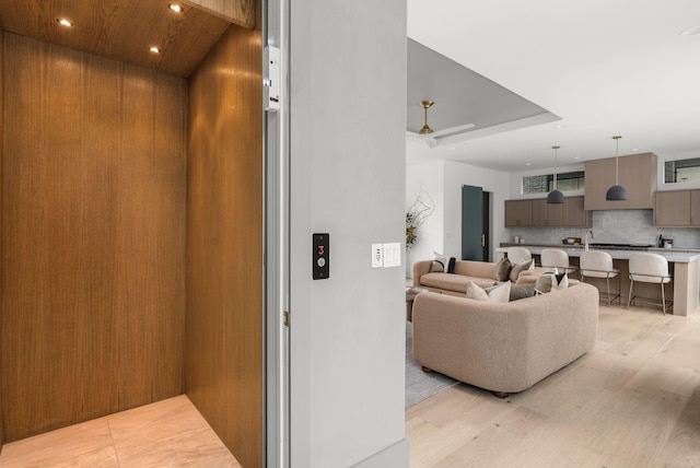 living room featuring light wood finished floors, recessed lighting, a raised ceiling, and elevator