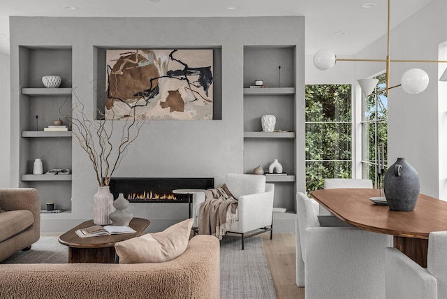 living room featuring a warm lit fireplace, built in features, and wood finished floors