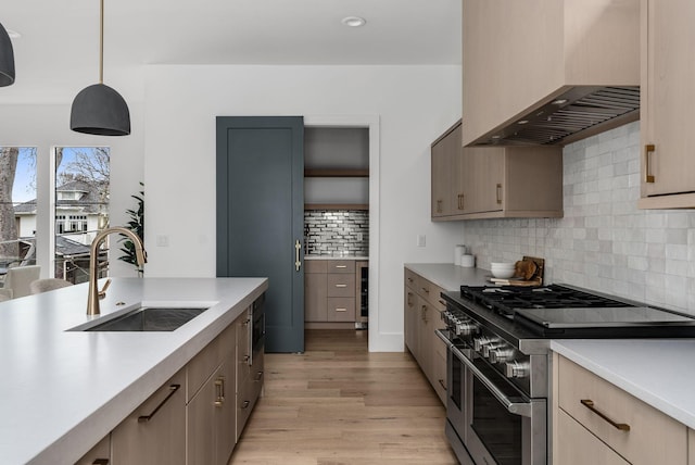 kitchen with light countertops, a sink, wall chimney range hood, light wood-type flooring, and double oven range