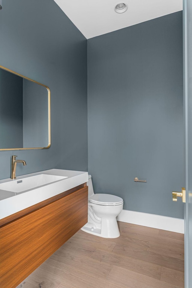 half bath with wood finished floors, vanity, toilet, and baseboards