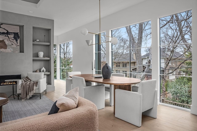 dining room with built in features, light wood-type flooring, and a warm lit fireplace