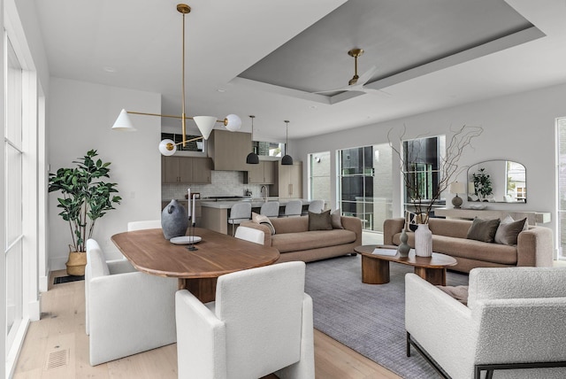 living room with light wood-type flooring, a tray ceiling, visible vents, and ceiling fan