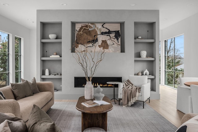 living area with a lit fireplace, wood finished floors, and built in features