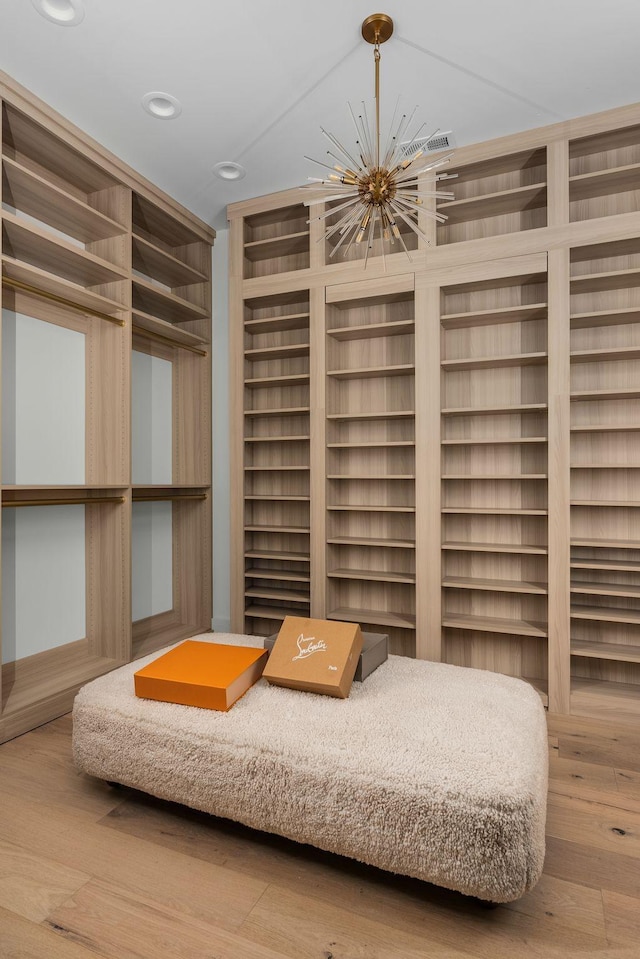 walk in closet with wood finished floors and an inviting chandelier