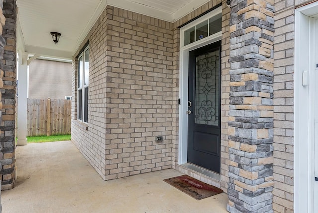 view of exterior entry featuring fence and brick siding