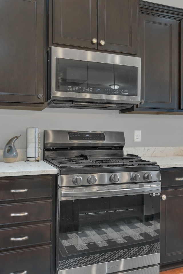 kitchen with stainless steel appliances, dark brown cabinetry, and light stone countertops