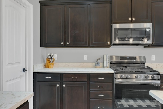 kitchen featuring stainless steel appliances, dark brown cabinets, and light stone counters