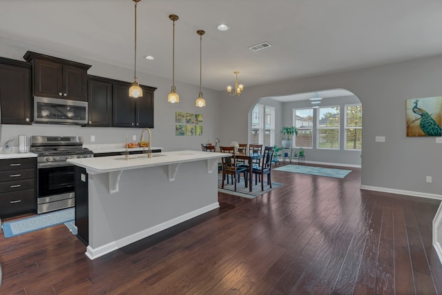 kitchen with dark wood-style floors, arched walkways, light countertops, appliances with stainless steel finishes, and a sink