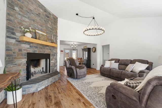 living area with high vaulted ceiling, a stone fireplace, wood finished floors, baseboards, and an inviting chandelier