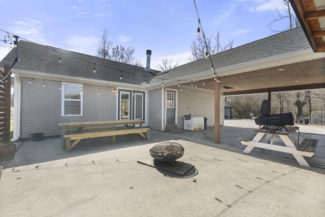 back of house featuring roof with shingles, a fire pit, and a patio