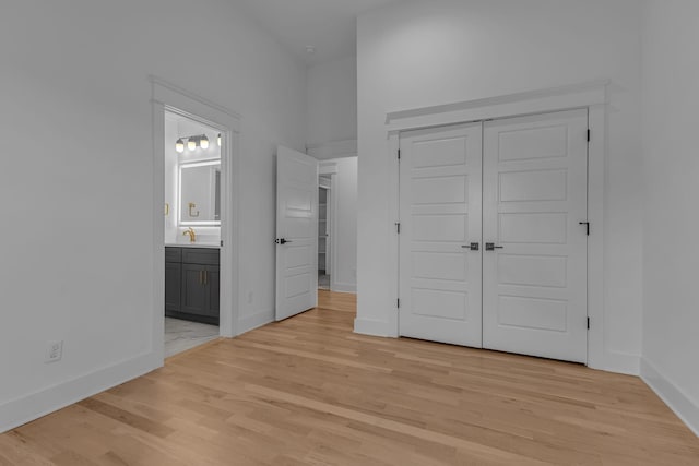 unfurnished bedroom with a closet, light wood-type flooring, a sink, and baseboards