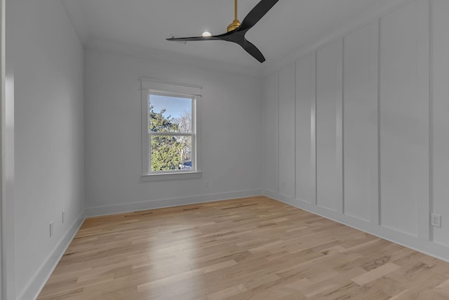 empty room with baseboards, ceiling fan, light wood-style flooring, crown molding, and a decorative wall