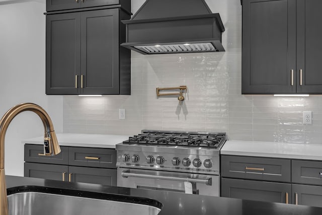 kitchen with a sink, high end stainless steel range, decorative backsplash, and custom range hood