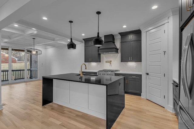 kitchen featuring decorative backsplash, coffered ceiling, light wood-style flooring, custom exhaust hood, and a sink