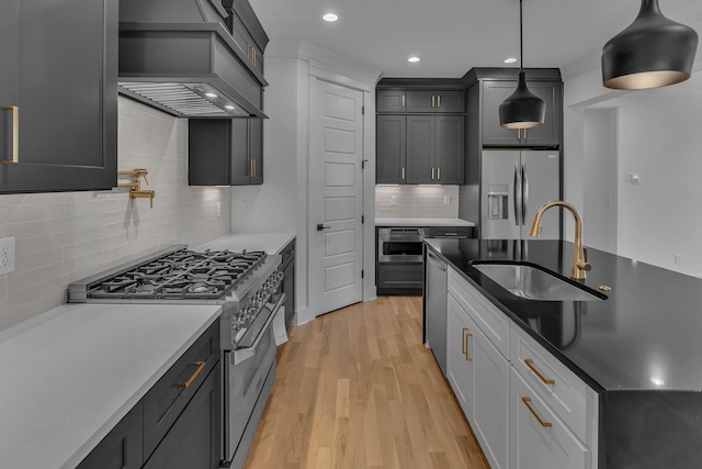 kitchen with stainless steel appliances, a sink, light wood-type flooring, custom exhaust hood, and pendant lighting