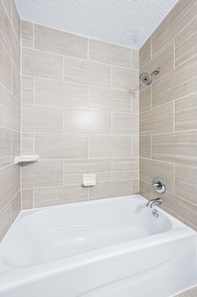 bathroom with a textured ceiling and bathing tub / shower combination