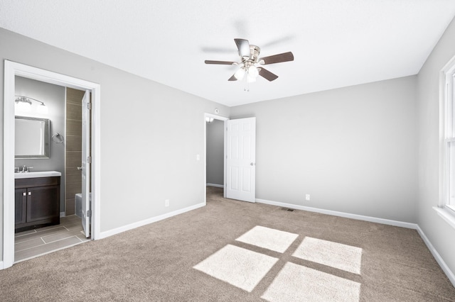 unfurnished bedroom with light carpet, baseboards, ensuite bath, ceiling fan, and a sink