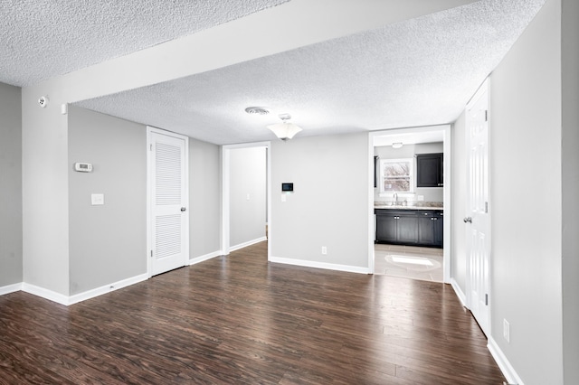 unfurnished living room featuring dark wood-style flooring, a sink, a textured ceiling, and baseboards