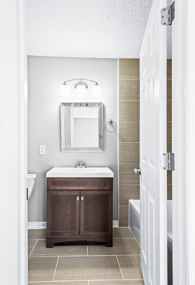 bathroom featuring a washtub, wood tiled floor, vanity, a textured ceiling, and baseboards