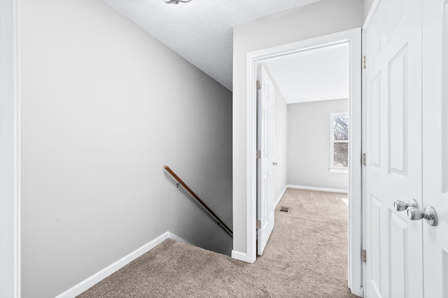 corridor with baseboards, visible vents, a textured ceiling, an upstairs landing, and carpet floors