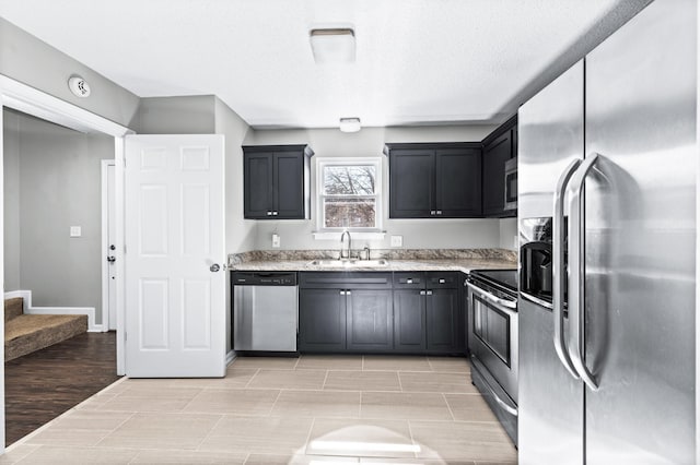 kitchen featuring a textured ceiling, stainless steel appliances, dark cabinetry, and a sink