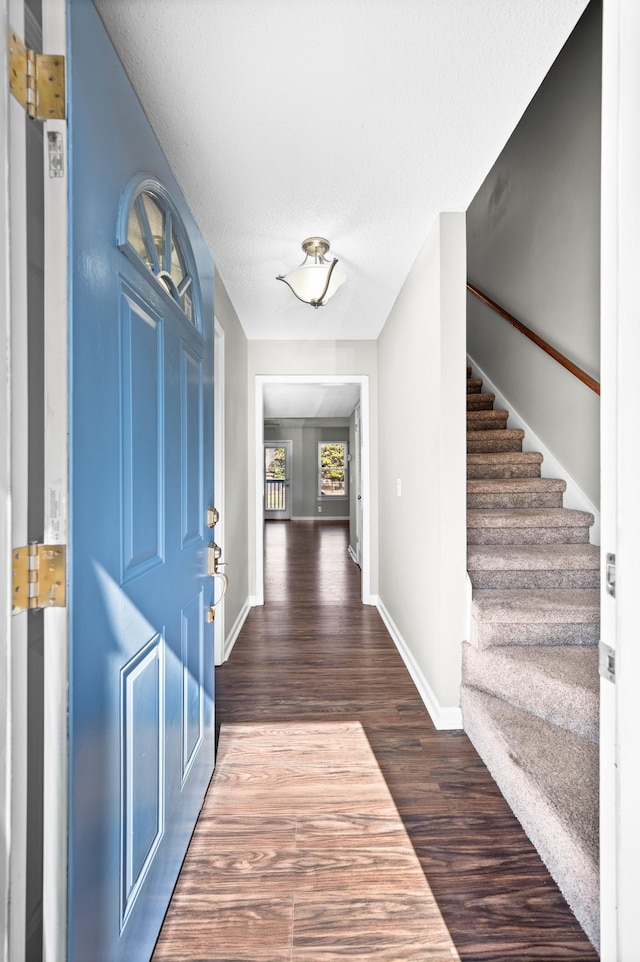 entryway featuring stairs, dark wood-type flooring, a textured ceiling, and baseboards