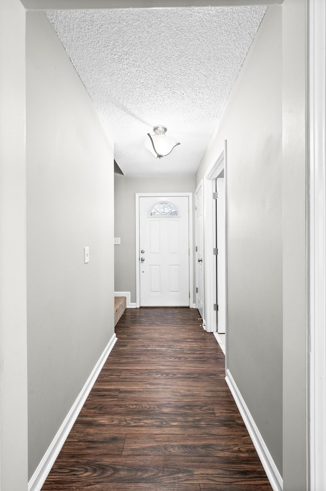 hall featuring a textured ceiling, baseboards, and dark wood-type flooring