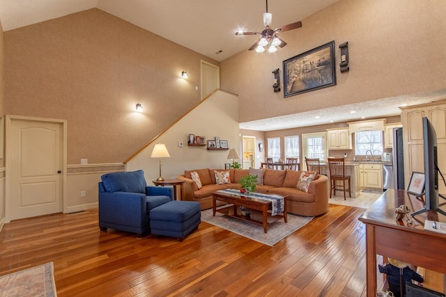 living area with high vaulted ceiling, light wood finished floors, and baseboards