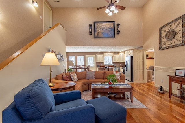 living room featuring visible vents, baseboards, a towering ceiling, ceiling fan, and light wood-type flooring