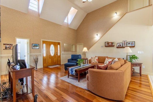 living area featuring light wood finished floors, baseboards, a skylight, and high vaulted ceiling