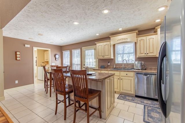 kitchen featuring light tile patterned floors, a kitchen island, appliances with stainless steel finishes, a kitchen bar, and a sink