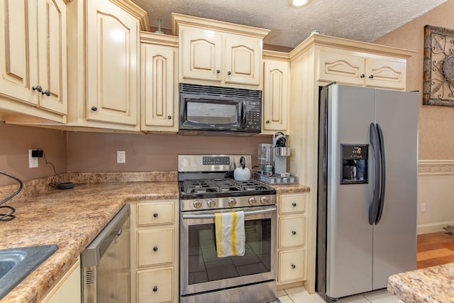 kitchen with stainless steel appliances, light countertops, cream cabinets, a sink, and a textured ceiling