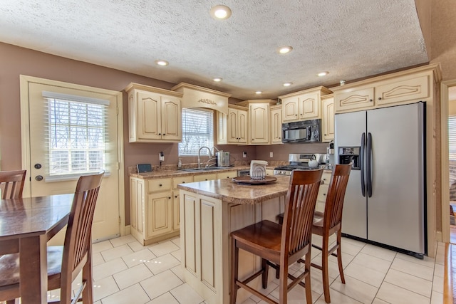 kitchen featuring light tile patterned floors, a breakfast bar area, appliances with stainless steel finishes, a center island, and a sink